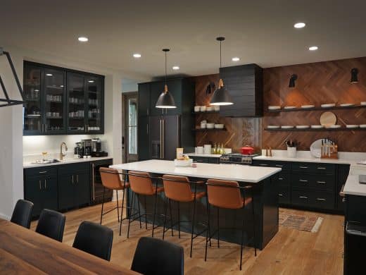 Modern kitchen with dark cabinets, white island, and a chevron wood-accent wall with open shelving and pendant lights.